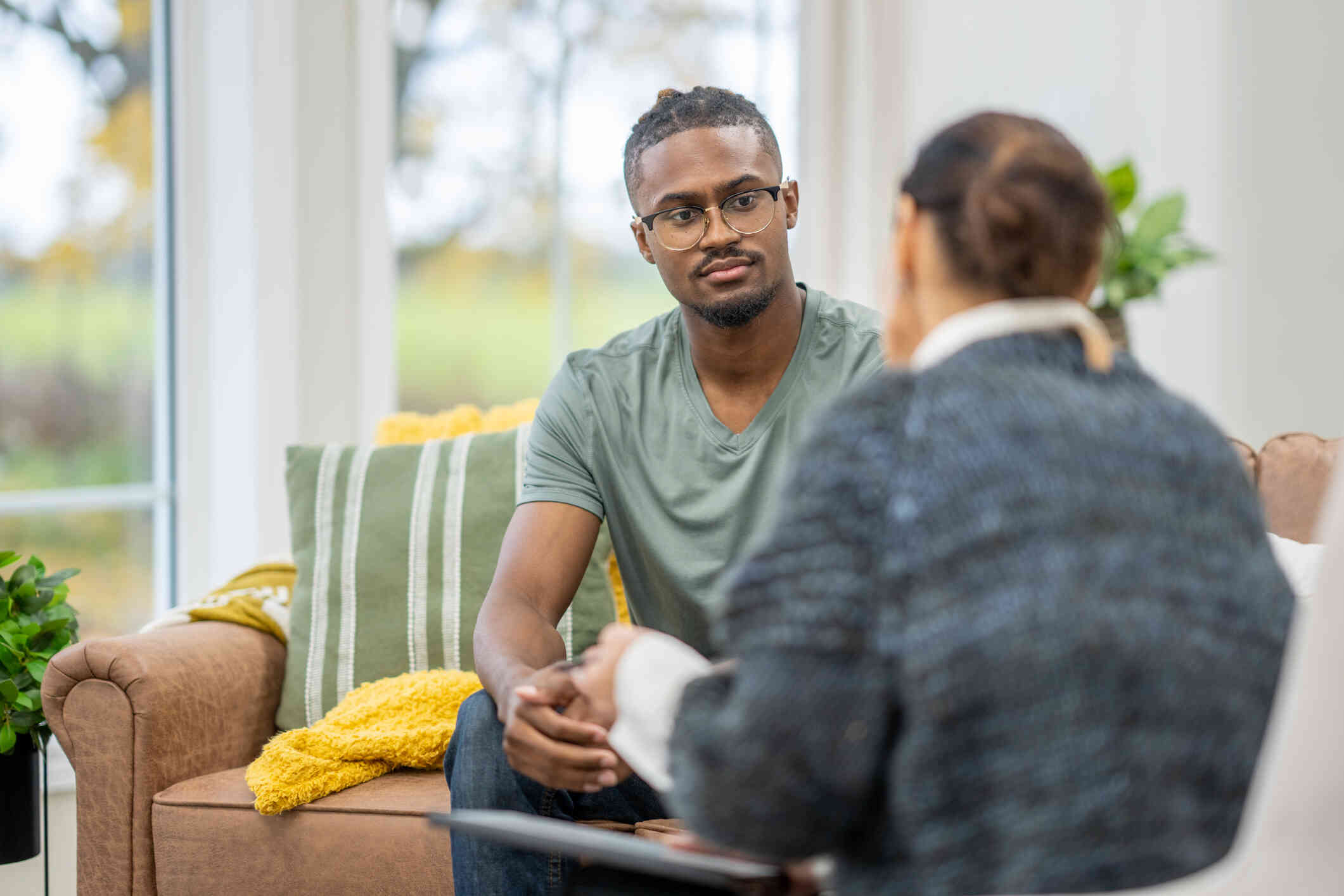 A man in agreen shirt sits across from his female therapist and listens to her talk during a therapy session.